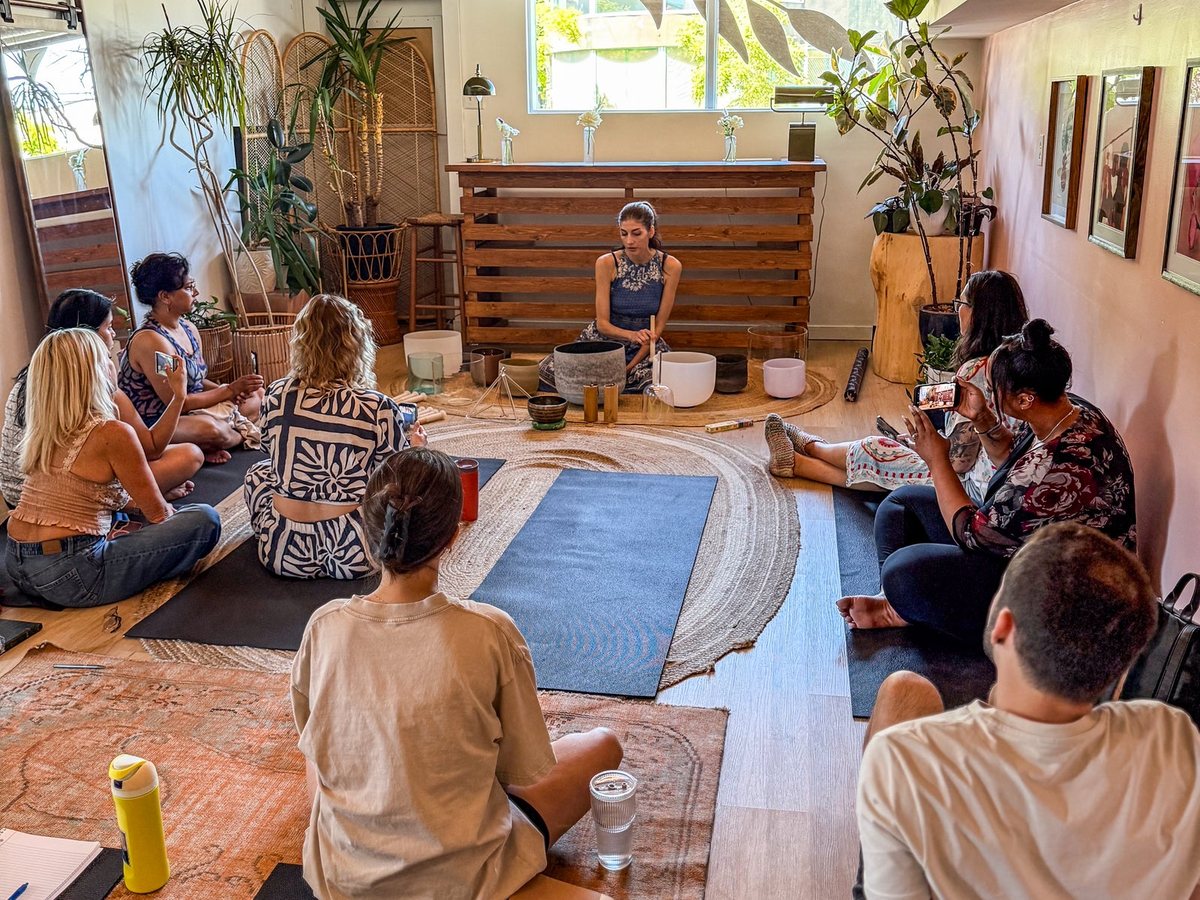 Students seated on mats in a circle around an instructor with crystal singing bowls during a Mystic Meditations training.